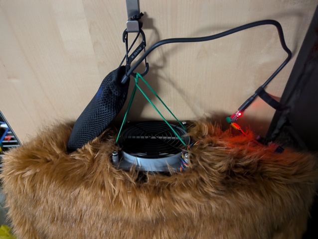 The fursuit dryer in use, hanging from a door hook on the carabiner with a bodysuit on it. A USB power bank feeds the 